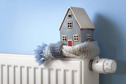 House model wrapped in scarf on radiator winter energy, heating and insulation background